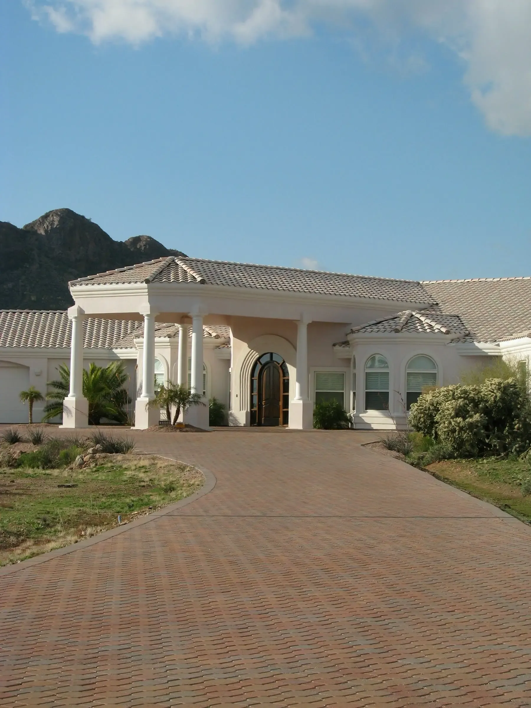 Paved drive up to the front entry of a stucco house, with desert mountains behind